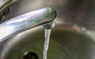 agua corriente de un grifo de agua en el desagüe de un fregadero de cromo. foto