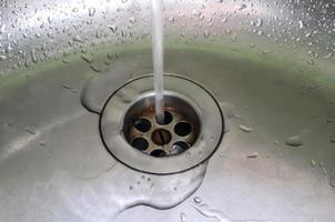 agua corriente de un grifo de agua en el desagüe de un fregadero de cromo. foto