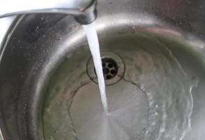 agua corriente de un grifo de agua en el desagüe de un fregadero de cromo. foto