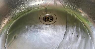 agua corriente de un grifo de agua en el desagüe de un fregadero de cromo. foto