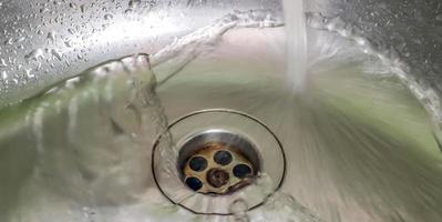 agua corriente de un grifo de agua en el desagüe de un fregadero de cromo. foto