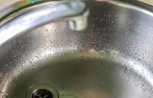 Running water from a water tap into the drain of a chrome sink. photo