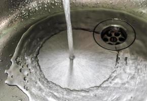 agua corriente de un grifo de agua en el desagüe de un fregadero de cromo. foto