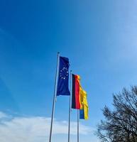 Flags of Ukraine, Germany and European Union fly side by side against blue sky. photo