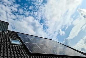 Solar panels producing clean energy on a roof of a residential house with cloud reflections.
