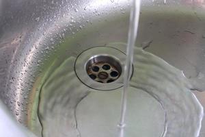 agua corriente de un grifo de agua en el desagüe de un fregadero de cromo. foto