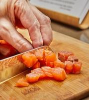 el chef corta el salmón en cubos con un cuchillo para preparar el plato según la receta