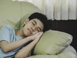 lindo niño asiático durmiendo y tomando una siesta en un sofá sobre una almohada con un dulce sueño después de aprender en línea. niño durmiendo concepto. foto