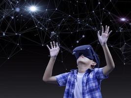 Boy wearing virtual reality glasses in modern interior design studio and trying to touch dots network and earth map or something appear in VR with exciting.Flares effect, blurred background concept. photo