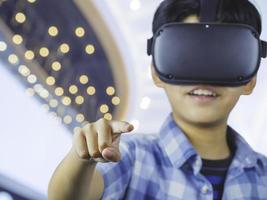 Kid wearing virtual reality glasses in modern interior design studio and trying to touch dots network and earth map or something appear in VR with exciting.Flares effect, blurred background concept. photo