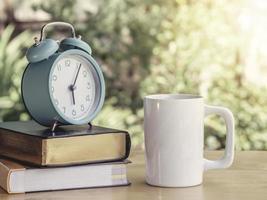 despertador en el libro de trabajo y libro de texto en la mesa o escritorio con café caliente en la oficina del hogar. negocio del lugar de trabajo y estilo de vida. foto