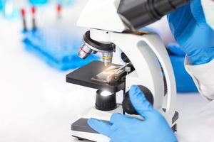 las manos de los hombres que usan guantes de goma azules están usando un microscopio para trabajar en el laboratorio.