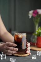 Hands holding a glass of espresso with lemon juice and fresh sliced lemon on wooden table and copy space, Summer Cocktail, Cold brew coffee or black tea. photo