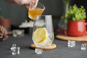 Glass of espresso with lemon juice and fresh sliced lemon on wooden table and copy space, Summer Cocktail, Cold brew coffee or black tea. Pouring cold drink. photo