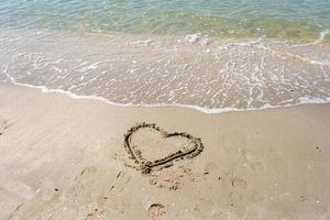 blurred of drawing heart on a yellow sand at a beautiful seascape background. Horizontal composition.