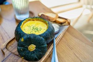 Roasted pumpkin cream soup in raw pumpkin serve with bread on rustic wooden background. photo