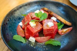 Summer salad with watermelon, tomatoes, feta cheese and basil on black plate in the wood table. photo
