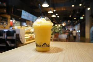 Mango fruity frappe, smoothies and shakes in plastic take away cup on the wooden table in beverage shop. photo