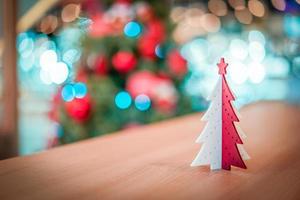 decoración de árbol de navidad de plástico rojo y blanco en la mesa de madera con un gran árbol de navidad borroso detrás. foto