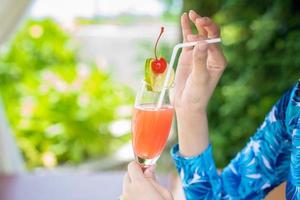 Asian woman relaxed on the beach with her red lime cherry cocktail in the hand in opening summer day photo