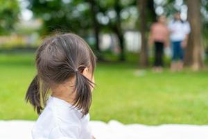 young girl looks back to her parent standing farway while she's plaing on the white mat in the garden. photo