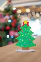 decoración artesanal de papel del árbol de navidad en la parte trasera en la mesa de madera con un gran árbol de navidad borroso detrás.