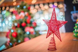 decoración de estrella roja en la mesa de madera con un gran árbol de navidad borroso detrás. foto