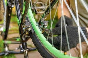 el mecánico de bicicletas repara la bicicleta en el taller de reparación de bicicletas, al aire libre. mano de ciclista ciclista examina, arregla sistema de transmisión de ciclo moderno. mantenimiento de bicicletas, concepto de tienda deportiva. foto