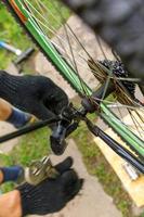 Bike mechanic man repairs bicycle in bicycle repair shop, outdoor. Hand of cyclist bicyclist examines, fixes modern cycle transmission system. Bike maintenance, sport shop concept. photo