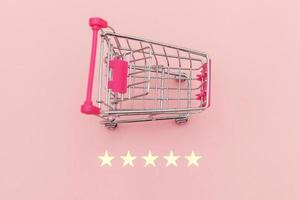 Small supermarket grocery push cart for shopping toy with wheels and 5 stars rating isolated on pastel pink background. Retail consumer buying online assessment and review concept. photo