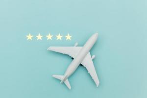 Simply flat lay design miniature toy model plane and 5 stars rating on blue pastel colorful trendy background. Travel by plane vacation summer weekend sea adventure trip journey ticket tour concept.