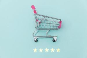 Small supermarket grocery push cart for shopping toy with wheels and 5 stars rating isolated on pastel blue background. Retail consumer buying online assessment and review concept. photo