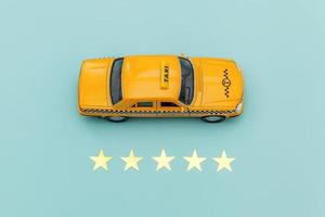 Yellow toy car Taxi Cab and 5 stars rating isolated on blue background. Smartphone application of taxi service for online searching calling and booking cab concept. Taxi symbol. Copy space. photo