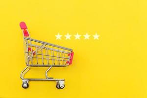 Small supermarket grocery push cart for shopping toy with wheels and 5 stars rating isolated on yellow background. Retail consumer buying online assessment and review concept. photo