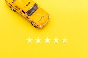 taxi de coche de juguete amarillo y calificación de 5 estrellas aislado sobre fondo amarillo. aplicación de teléfono inteligente del servicio de taxi para buscar en línea llamadas y reservar el concepto de taxi. símbolo de taxi. copie el espacio foto