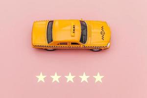 taxi de coche de juguete amarillo y calificación de 5 estrellas aislado sobre fondo rosa. aplicación de teléfono inteligente del servicio de taxi para buscar en línea llamadas y reservar el concepto de taxi. símbolo de taxi. copie el espacio foto