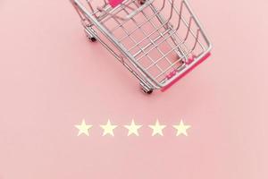 Small supermarket grocery push cart for shopping toy with wheels and 5 stars rating isolated on pastel pink background. Retail consumer buying online assessment and review concept. photo