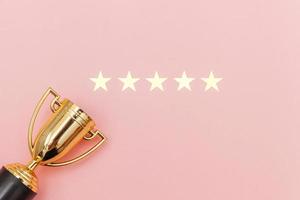 Simply flat lay design winner or champion gold trophy cup and 5 stars rating isolated on pink pastel background. Victory first place of competition. Winning or success concept. Top view copy space. photo