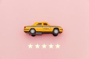 taxi de coche de juguete amarillo y calificación de 5 estrellas aislado sobre fondo rosa. aplicación de teléfono inteligente del servicio de taxi para buscar en línea llamadas y reservar el concepto de taxi. símbolo de taxi. copie el espacio foto