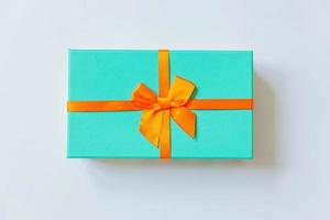 navidad año nuevo cumpleaños san valentín celebración presente concepto romántico. caja de regalo azul de diseño minimalista con cinta naranja aislada en fondo blanco. espacio de copia de vista superior plana.