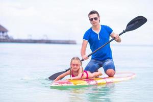 la niña y el joven papá se divierten en la tabla de surf foto