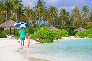 Father and little girl with umbrella hiding from sun at beach photo