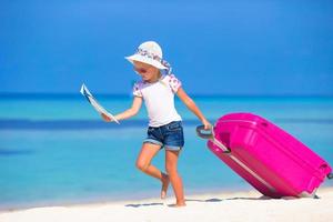 niña adorable con una maleta grande en una playa blanca tropical