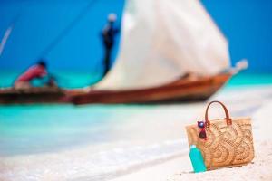Beach accessories - straw bag, sunscreen bottle and red sunglasses on the beach photo