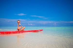 Little adorable girl on a surfboard in the turquoise sea photo