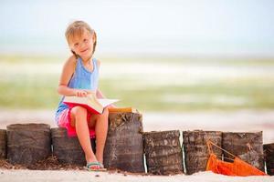 Little adorable girl reading book during tropical white beach photo