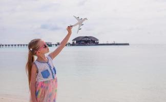 Happy little girl with toy airplane in hands on white sandy beach photo