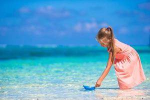 Adorable little girl playing with origami boat in turquoise sea