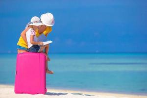 Mother and little daughter with luggage and map on beach photo