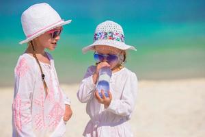 Little girl drinking mineral bottle of water at hot summer day on beach photo
